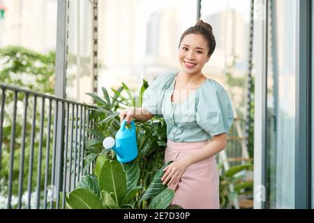 Portrait der schönen Frau Gießen grünen Pflanzen auf dem Balkon, kleinen gemütlichen Garten in der Wohnung Stockfoto