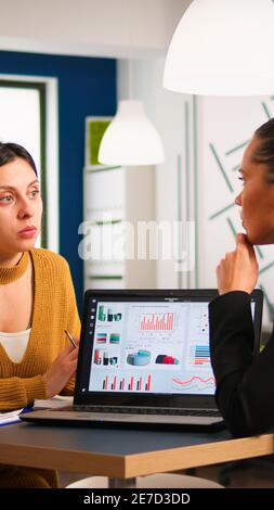 Junge multikulturelle Arbeiter sprechen, betrachten Laptops und analysieren digitale Daten, die am Schreibtisch sitzen. Professionelle Kollegen Team diskutieren Projekt mit Geräten in der Unternehmensniederlassung. Stockfoto