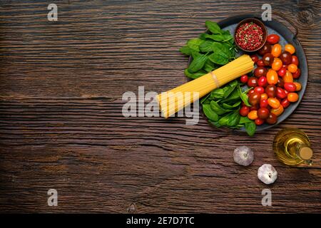 Draufsicht auf ein Bündel von rohen Spaghetti mit Spinat, Tomaten, Knoblauch und Olivenöl Stockfoto
