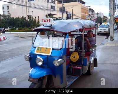 Ein Thai Tuk Tuk oder Taxifahrer wartet auf Passagiere, die beim Lesen der Zeitung ankommen Stockfoto