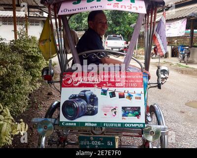 Ein alter Mann, ein Pediküre-Fahrer, lächelt in seiner Rikscha, die von einer Kamera gesponsert wird Stockfoto