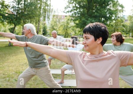 Reife Frau trainiert zusammen mit ihrer Gruppe während des Sporttrainings Im Park im Freien Stockfoto