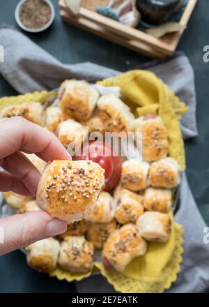 Nahaufnahme einer gebackenen hausgemachten Wurstrolle, die von einer Frau gehalten wird, überreichen ein verschwommenes Gericht voller Würstchen, die gerade gebacken wurden. Stockfoto