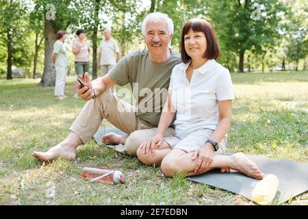 Porträt eines älteren Paares, das während des Sitzens auf die Kamera schaut Grünes Gras und Training im Park Stockfoto