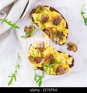Rührei und gebratene Pilze auf Brot. Hausgemachtes Frühstück oder Brunchmenü - Rühreier und Pilze Sandwiches. Draufsicht, Overhead, Copy SPA Stockfoto