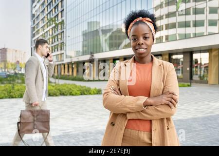 Porträt einer jungen afrikanischen Frau, die mit der Kamera lächelt Ihre Arme kreuzten sich in der Stadt Stockfoto