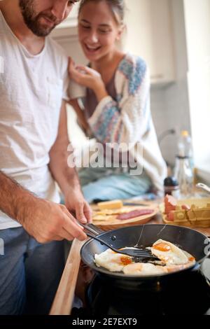 Ein junges Mädchen mag das Frühstück von ihrem Freund an einem schönen Morgen zubereitet. Kochen, zusammen, Küche, Beziehung Stockfoto