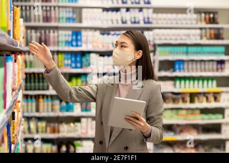 Junge asiatische weibliche Verbraucher mit Tablet stehen im Regal mit Körperpflegeprodukte und die Wahl eines für sich selbst bei der Verwendung des Touchpads Stockfoto