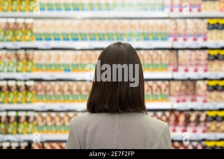Rückansicht der jungen Brünette weibliche Verbraucher stehen durch große Regal mit kosmetischen Produkten und Blick auf sie bei der Auswahl Eins für sich Stockfoto