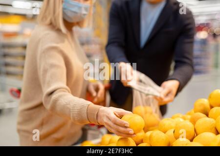 Reifes Paar in Casualwear und Schutzmasken Auswahl frisch reif Mandarinen im Supermarkt, während die Frau einen aus dem Display nimmt Stockfoto