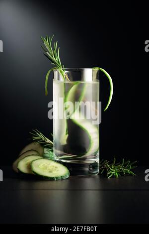 Kaltes Erfrischungsgetränk mit Eis, Gurke und Rosmarin. Das gefrorene Glas auf einem schwarzen Tisch. Stockfoto