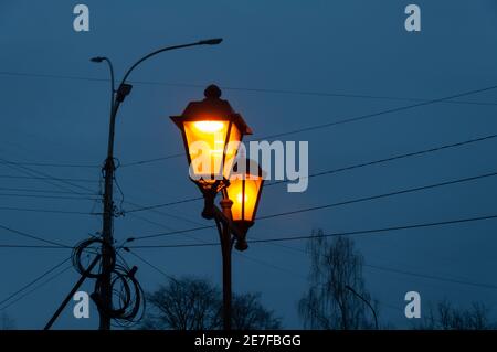 Ein alter Laternenpfosten mit brennenden Lampen, blauer Himmel in der Dämmerung Stockfoto