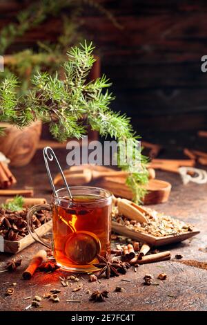 Weihnachtlicher Kräutertee mit Zimt, Anis und getrockneten Kräutern. Kräutertee mit Wacholderzweig auf einem alten braunen Tisch. Stockfoto