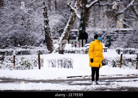 Berlin, Deutschland. Januar 2021. Deutschland, Berlin, 30. Januar 2021: Eine Frau mit Gesichtsmaske im gelben Mantel ist im Neuschnee im Volkspark Schöneberg-Wilmersdorf zu sehen. (Foto: Jan Scheunert/Sipa USA) Quelle: SIPA USA/Alamy Live News Stockfoto