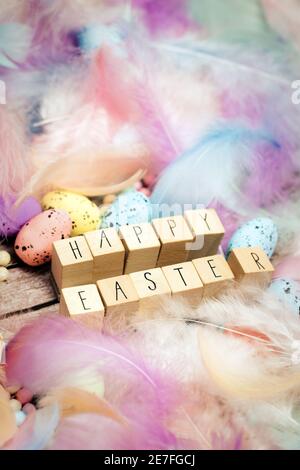 Frohe Ostern geschrieben mit Holzwürfeln umgeben von schönen pastellfarbenen dekorativen Federn und Eiern, April, Ostern, Religion, Frühlingskonzept Stockfoto