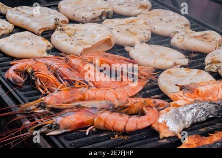 Prozess der Zubereitung von roten Kaisergranat-Garnelen, Tintenfischen, Lachssteaks auf dem Grill Stockfoto