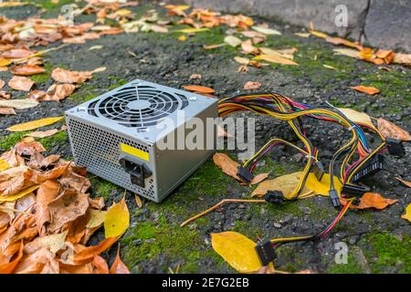 Die Stromversorgung eines PCs liegt in einem Elektronikkippe unter Herbstblättern Stockfoto