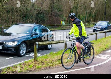 Ein Erwachsener Mann Radfahren auf einem Radweg Blick auf den Verkehr, wie er versucht, die Hauptstraße wieder zu verbinden. Der Radfahrer trägt eine gut sichtbare Jacke und einen Helm. Stockfoto