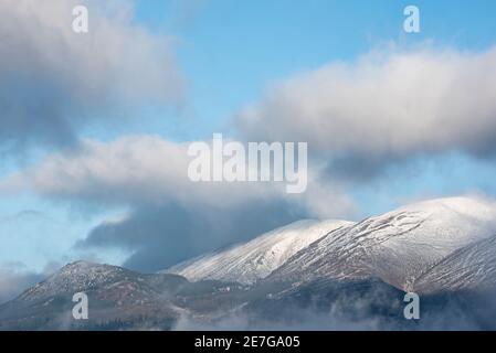 Atemberaubende Landschaft Bild von Skiddaw schneebedeckten Bergkette in Lake District im Winter mit niedrigen Wolken um Gipfel Stockfoto