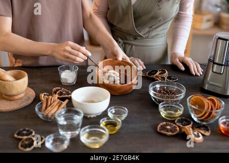 Junge Frau mischen gemahlene kandierte Früchte in Holzschüssel während Stehen am Tisch mit Zutaten für die Herstellung von Naturseife Stockfoto