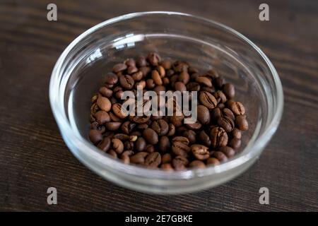 Glasschale mit gerösteten Kaffeebohnen auf Holztisch vorbereitet Zum Mahlen vor der Herstellung von hausgemachten Naturkosmetikprodukten Stockfoto