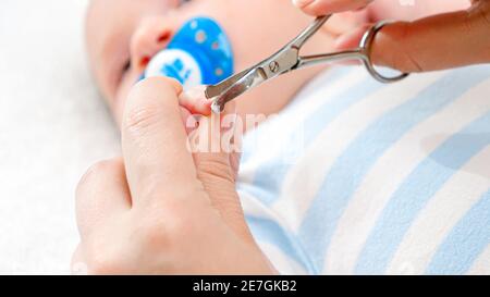 Nahaufnahme des Schneidens neugeborener Fingernägel mit einer speziellen Schere. Konzept von Babys und Neugeborenen Hygiene und Gesundheitsversorgung. Fürsorgliche Eltern mit wenig Stockfoto