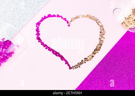 Herzform aus mehrfarbigem Glitzer. Zwei Sektgläser mit herzförmigem Konfetti auf Glitzerhintergrund. Valentinstag-Konzept. Stockfoto