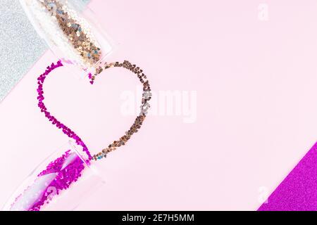 Herzform aus mehrfarbigem Glitzer. Zwei Sektgläser mit herzförmigem Konfetti auf Glitzerhintergrund. Valentinstag-Konzept. Stockfoto