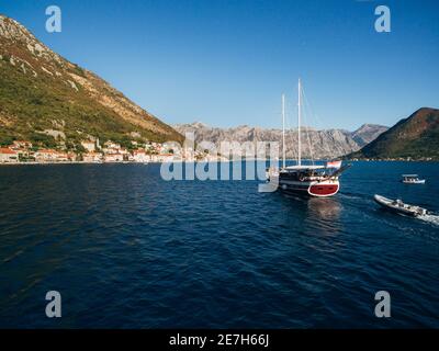 Eine große Segelyacht aus Holz segelt vor der Kulisse der Stadt Perast in Montenegro. Stockfoto