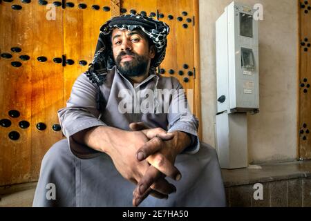 Saudi-arabische Männer sitzen vor dem geschlossenen Laden in Al Hasa, Saudi-Arabien. Stockfoto