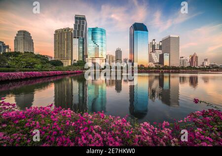 See mit violetten Blumen im City Park unter Wolkenkratzern bei Sonnenuntergang. Benjakiti Park in Bangkok, Thailand Stockfoto