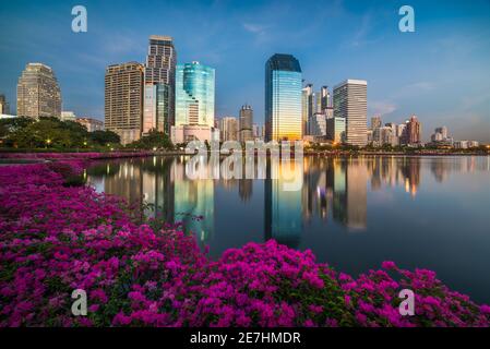 See mit violetten Blumen im City Park unter Wolkenkratzern in der Dämmerung. Benjakiti Park in Bangkok, Thailand Stockfoto
