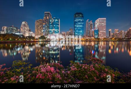 See mit lila Blumen im City Park unter Wolkenkratzern in der Nacht. Benjakiti Park in Bangkok, Thailand Stockfoto