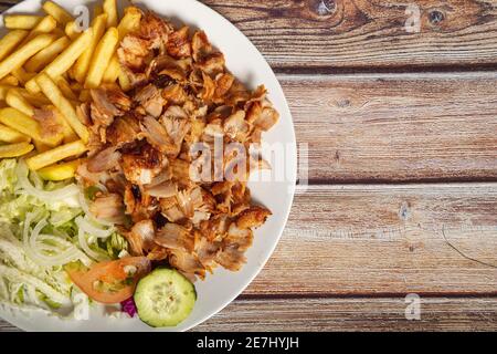Hühnerdöner auf einem Teller mit pommes Frites und Salat Auf Holzhintergrund mit Platz für Text Stockfoto