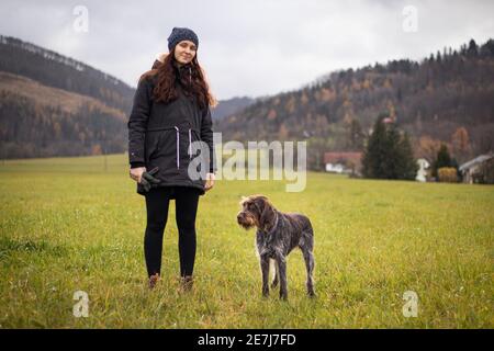 Faszinierte Gesicht einer braunen weiblichen Bohemian Wire-haired zeigt Griffon. Besitzer in Winterkleidung mit einem leichten Lächeln. Das Konzept der Beziehung Stockfoto