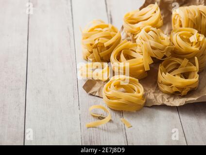 Hausgemachte Tagliatelle Pasta in braunem Papier auf weißem Holzhintergrund. Stockfoto