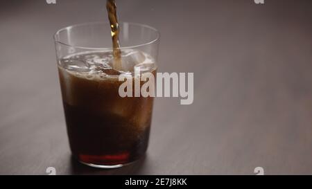 Gießen Sie Cola über Eiswürfel in Glas auf Walnusstisch mit Kopierraum, breites Foto Stockfoto