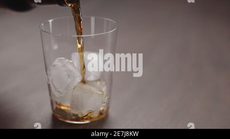 Gießen Sie Cola über Eiswürfel in Glas auf Walnusstisch mit Kopierraum, breites Foto Stockfoto