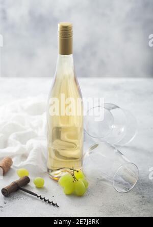 Leere Gläser und eine Flasche Sommer Weißwein mit Trauben, Korken und Korkenzieher auf hellem Tischhintergrund. Stockfoto
