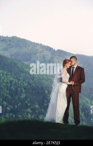Happy stilvolle Braut und Bräutigam laufen und Spaß in den Bergen am sonnigen Sommertag. Wunderschöne neuvermählte Paar lachen, wahre Gefühle. Emotional rom Stockfoto