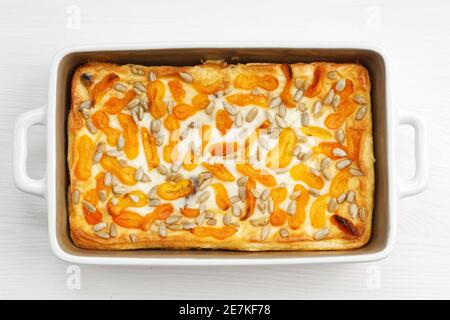 Hausgemachter Hüttenkäse-Auflauf mit getrockneten Aprikosen und Sonnenblumenkernen auf weißem Holztisch. Draufsicht. Stockfoto