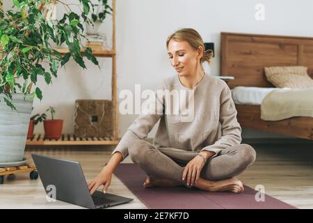 Schöne blonde junge Frau in bequemen Sport tragen Praxis Yoga Im gemütlichen Schlafzimmer zu Hause Stockfoto