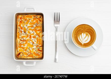 Tasse Kaffee und hausgemachter Hüttenkäse-Auflauf mit getrockneten Aprikosen und Sonnenblumenkernen auf weißem Holztisch. Draufsicht. Stockfoto