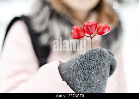 Das Mädchen hält in ihren Händen, die in Fäustlingen sind, einen Strauß roter Herzen. Das Konzept des Valentinstag. Stockfoto