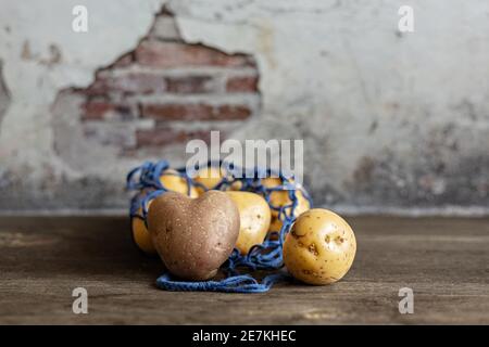 Herzförmige rote Kartoffeln mit weißen Kartoffeln in einem blauen Öko-Gitter auf einem Holzhintergrund Nahaufnahme. Stockfoto