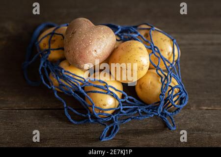 Herzförmige rote Kartoffeln mit weißen Kartoffeln in einem blauen Öko-Gitter auf einem Holzhintergrund Nahaufnahme. Stockfoto