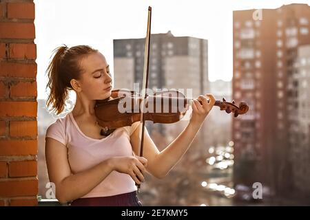 Ein junges Mädchen, eine Musikerin, spielt auf dem Balkon ihrer Wohnung Geige. Stockfoto