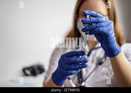 Eine Ärztin, die eine medizinische Maske trägt, zieht den Coronavirus-Impfstoff in eine Spritze in der Klinik.das Konzept der Impfung, Immunisierung, Prävention Stockfoto
