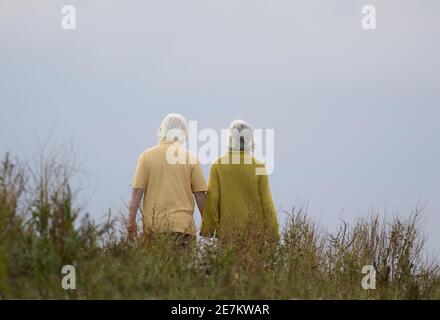 Ein älteres Paar geht Hand in Hand an einem bewölkten Tag, Norfolk, Großbritannien Stockfoto