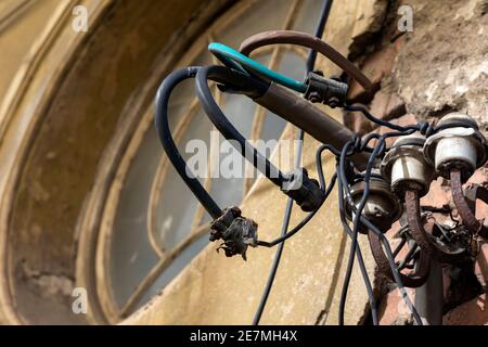 Drei altmodische altmodische Keramik-Isolatoren für eine handgefertigte elektrische Leitung An einer alten beschädigten Wand montiert Stockfoto